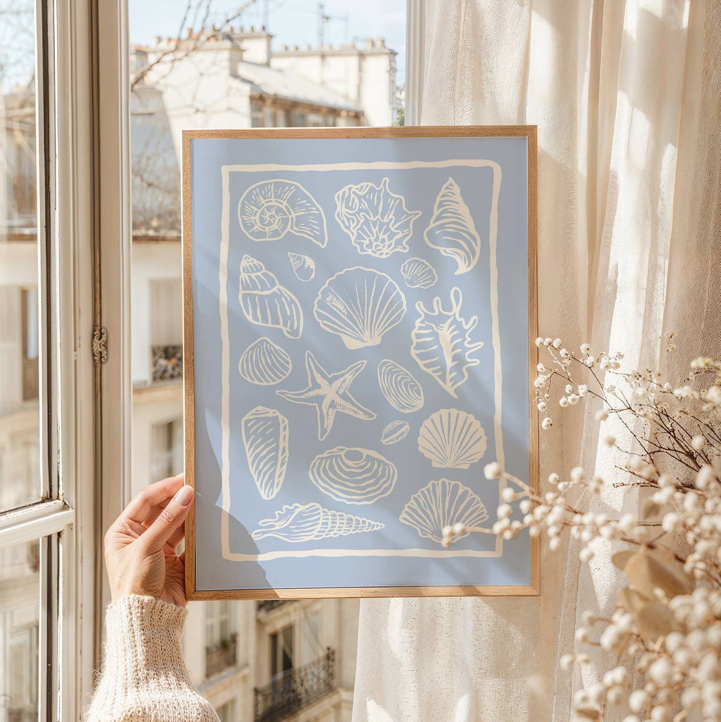 Framed artwork with shell patterns held by a person in front of a window.