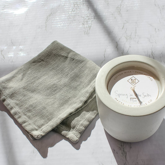 On a marble counter, sits a white concrete candle next to a grey washcloth. The candle is Spring in the South scent.