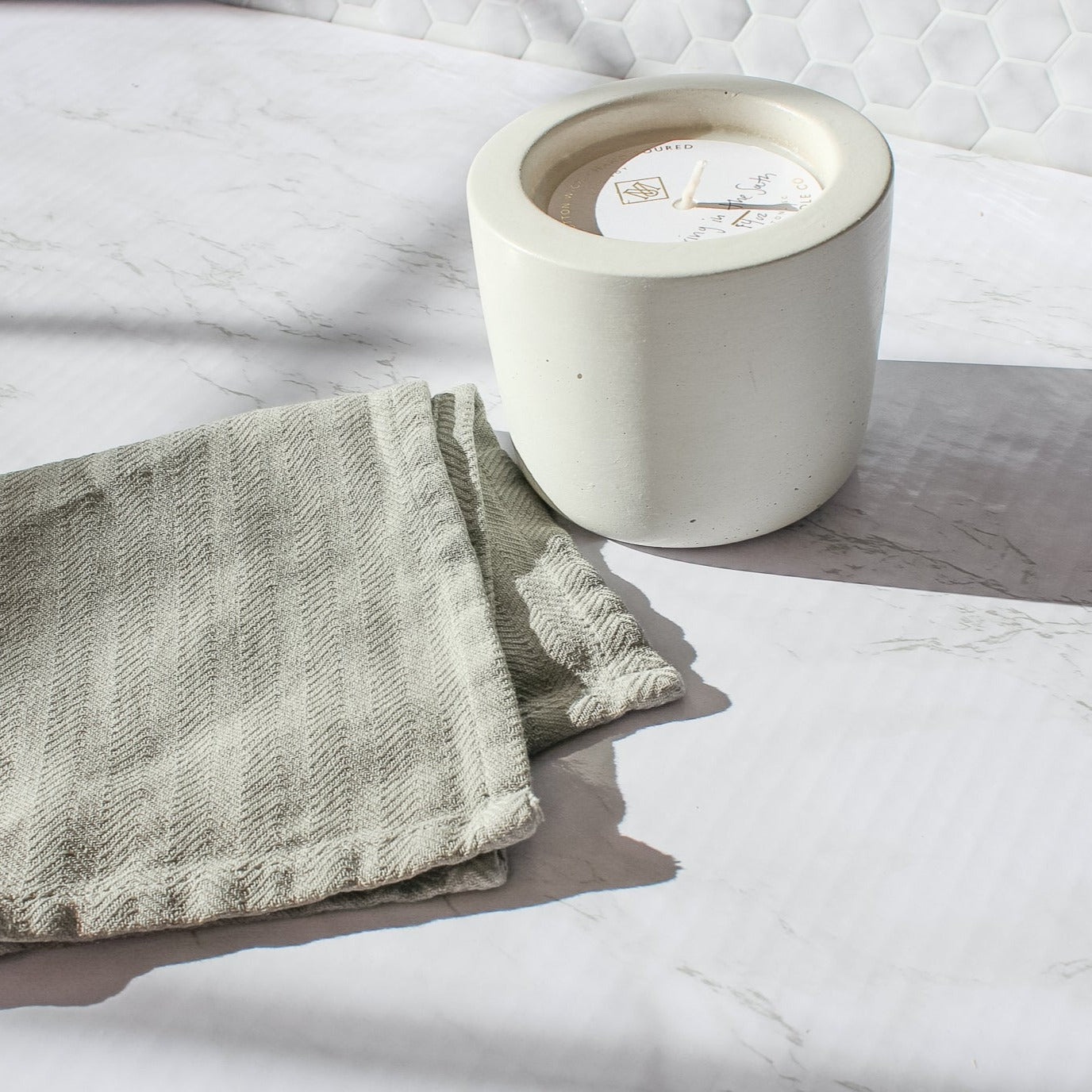 On a marble counter, sits a white concrete candle next to a grey washcloth. The candle is Spring in the South scent.