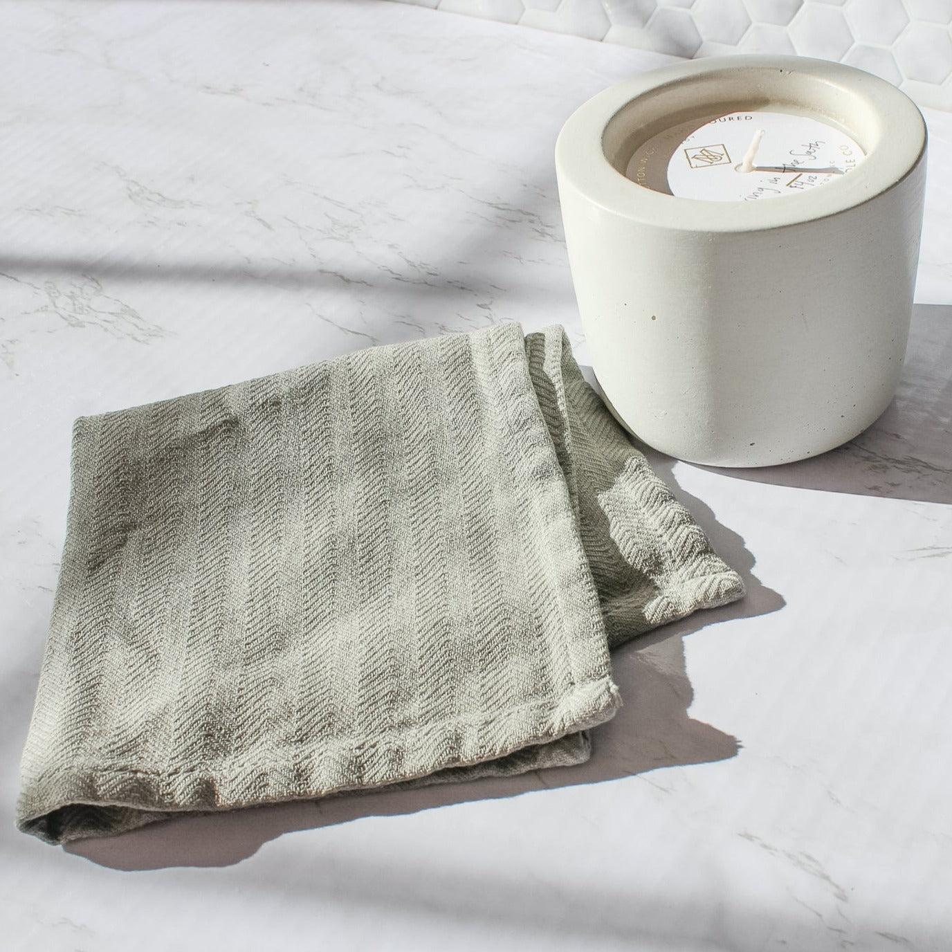 On a marble counter top sits our grey wash cloth next to our white cement candle in spring in the south scent.