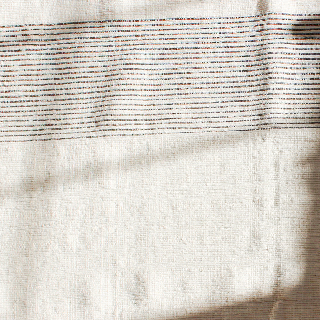 Zoomed in view of the woven bath mat. Cream with navy stripes on about 1/3 of the mat going horizotally