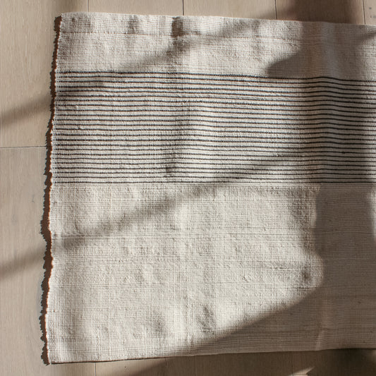 Cream bathmat with navy stripes on about 1/3 of the mat going horizontally.