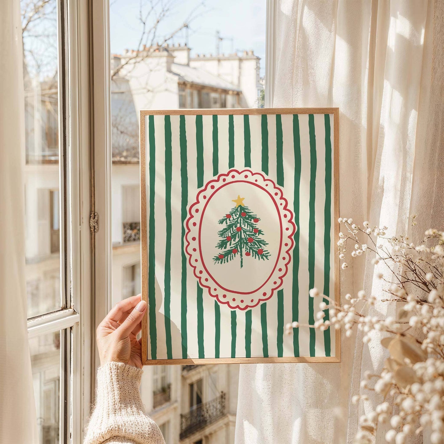 Framed artwork with a Christmas tree design held by a person in front of a window.