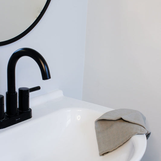 Our grey wash cloth sits on the side of a white sink.