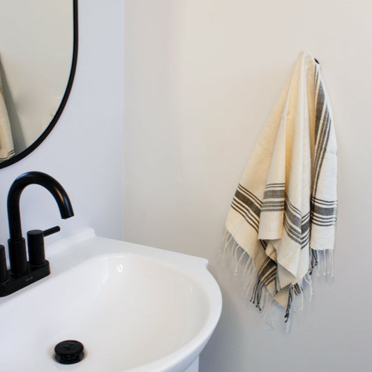 A natural colored towel with grey hatch striped pattern hanging on a bathroom towel hook.
