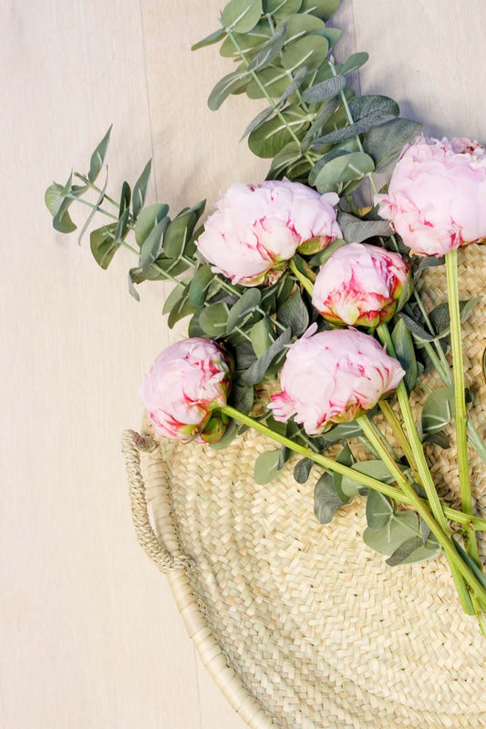 Large woven plate with handles holds eucalyptus branches and pink peonies