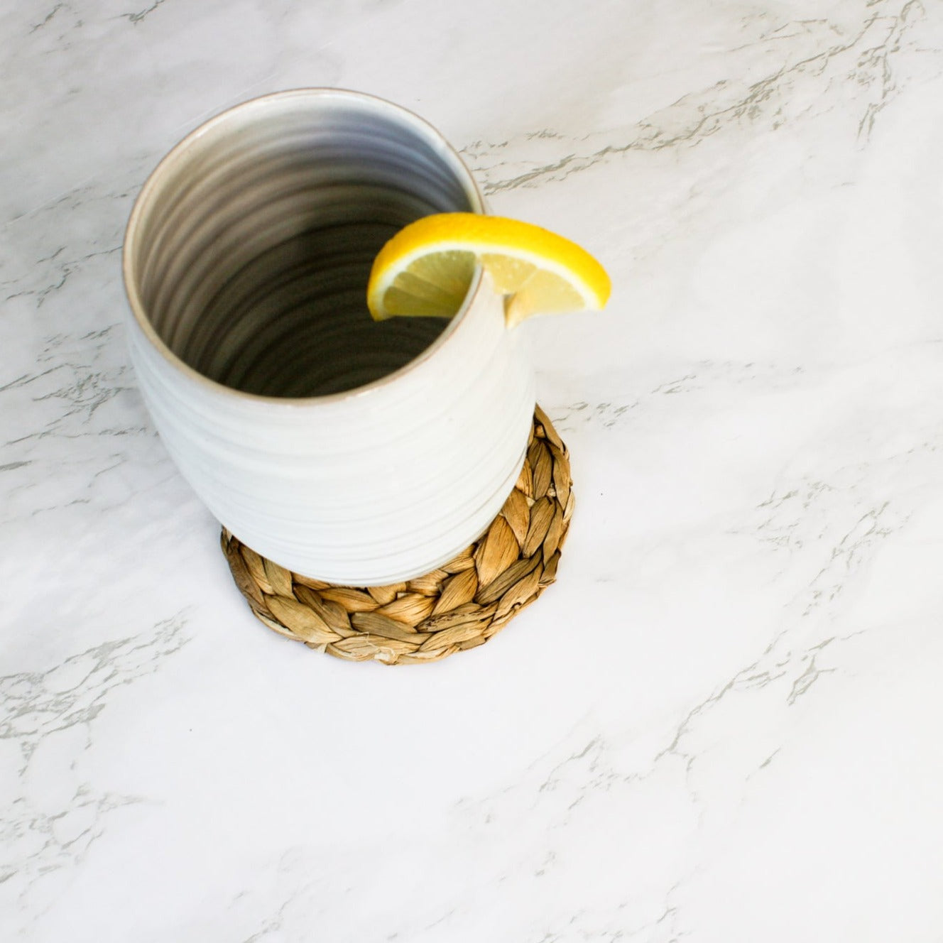 On a marble countertop, our tall tumbler sits on one of our round seagrass coasters.